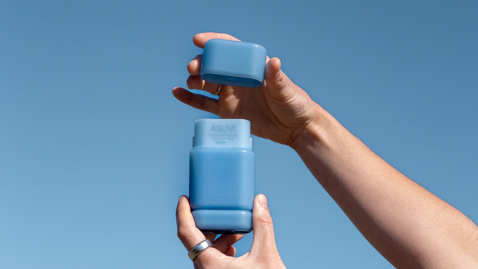 Two hands holding blue containers against a clear blue sky